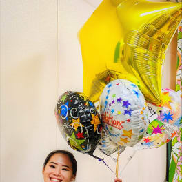 Person smiling and holding a bunch of colorful congratulatory mylar balloons including a large gold star.