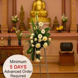 Tall white floral easel spray with greenery in a temple setting and a sign noting advance order time.