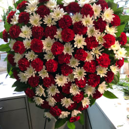 Heart-shaped floral spray of red carnations and white daisies on a stand