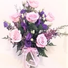 Pink and purple rose bouquet in a clear glass vase with a pink ribbon