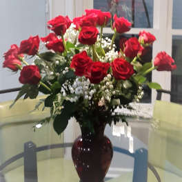 Red roses arranged in a dark glass vase with white filler flowers