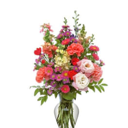 Tall mixed bouquet of pink roses, carnations, and purple asters in a clear glass vase