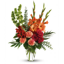 Tall arrangement of orange gladiolus, red roses, and peach carnations in a clear glass vase