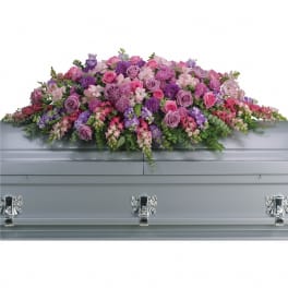 Lavender and pink casket spray with roses, snapdragons, and other flowers on a gray casket