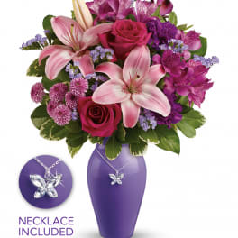 Pink lilies and roses with purple flowers in a purple vase with a butterfly necklace.