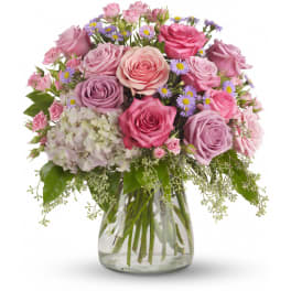 Pink and lavender rose arrangement with white hydrangea and purple asters in a clear glass vase