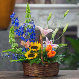 Basket arrangement with sunflowers, lilies, and blue flowers