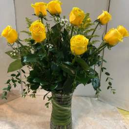 Yellow roses arranged in a clear glass vase with greenery