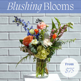 Mixed bouquet in a clear glass vase with blue, pink, orange, and white blooms
