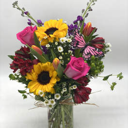 Mixed bouquet with sunflowers, pink roses, and a butterfly in a glass vase