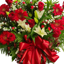 Red roses and gerbera daisies with white lilies and a red ribbon bow