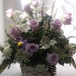Lavender roses in a woven basket with white filler flowers