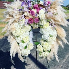 Large floral funeral spray with white hydrangeas, purple roses, and pampas grass