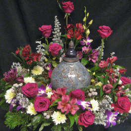 Floral arrangement with pink roses and mixed blooms around a decorative urn