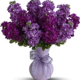Purple flower bouquet in a lavender vase with a ribbon bow