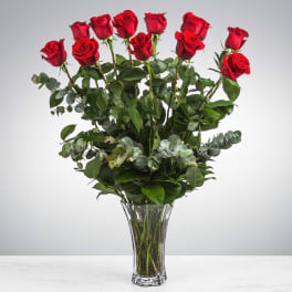Tall arrangement of long-stem red roses with eucalyptus in a clear glass vase