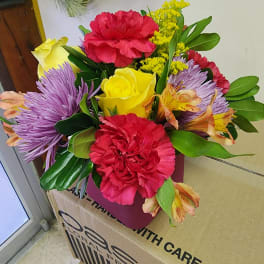 Mixed bouquet with red carnations, yellow roses, and purple flowers in a pink box