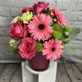 Pink roses and gerbera daisies arranged in a purple vase
