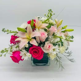 Mixed bouquet of pink roses, lilies, and white daisies in a square glass vase