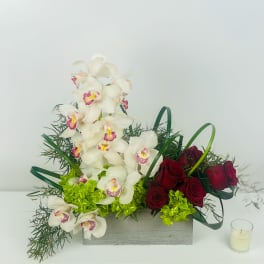 White orchids and red roses arranged in a rectangular box with a small candle beside it.