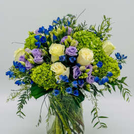 Bouquet of blue, lavender, and white flowers in a clear glass vase