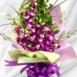Bouquet of purple orchids wrapped in pink and green paper with a purple ribbon