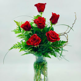 Red roses arranged in a clear glass vase with green foliage