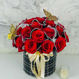 Red roses arranged in a black round box with a cream ribbon