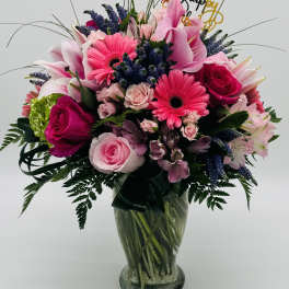 Mixed pink and purple bouquet in a glass vase with a Happy Birthday topper