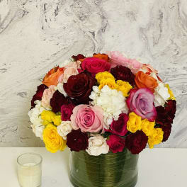 Mixed roses in a green glass vase beside a small candle