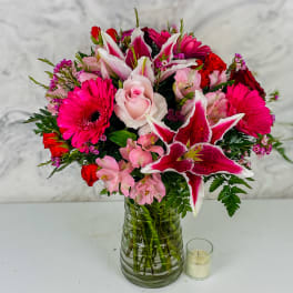 Pink and red mixed bouquet in a glass vase with a small candle beside it