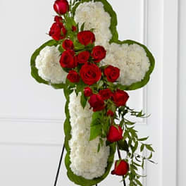 Cross-shaped floral tribute with red roses and white flowers on a stand