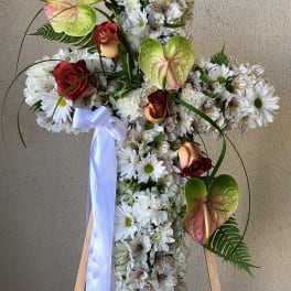 Cross-shaped floral tribute with white daisies and red roses on an easel