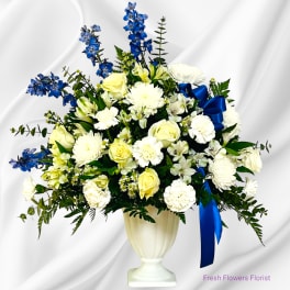 White and yellow floral arrangement with blue flowers in a white urn vase