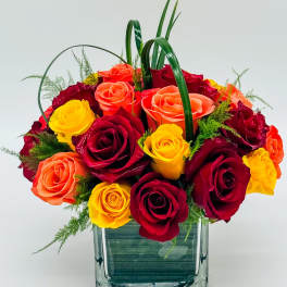 Bouquet of red, yellow, and orange roses in a square glass vase