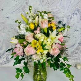 Mixed bouquet of pink roses, white lilies, and yellow flowers in a glass vase