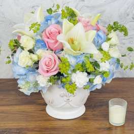 Pink roses and white lilies arranged in a white vase with blue flowers
