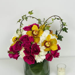 Magenta roses and yellow orchids in a green glass vase with ivy arches