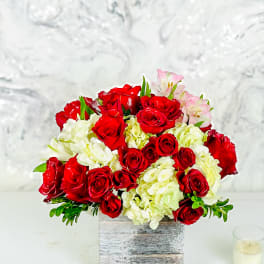 Red roses and white hydrangeas in a square wooden vase with pink lilies