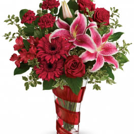 Red roses and pink lilies in a clear vase with red ribbon