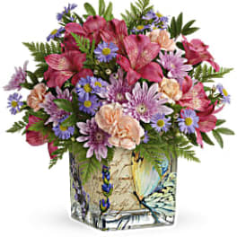 Mixed bouquet of pink, purple, and peach flowers in a decorative square vase