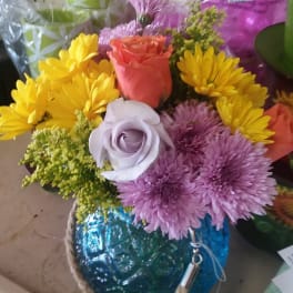 Mixed bouquet with roses and daisies in a blue glass vase