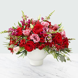 Red and pink rose arrangement in a white vase
