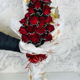 Tall bouquet of red roses wrapped in white paper with a red bow