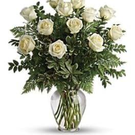 White roses arranged in a clear glass vase with greenery