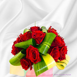 Bouquet of red roses with green and yellow leaf wraps in a pink box