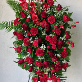 Tall standing spray of red flowers with greenery on a black easel