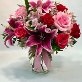 Pink and red roses with lilies in a clear glass vase