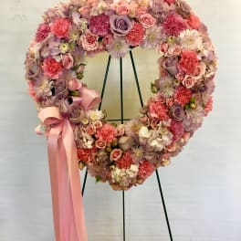 Heart-shaped floral wreath with pink and lavender blooms and a pink ribbon