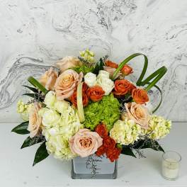 Mixed bouquet of peach, orange, and white roses in a square glass vase